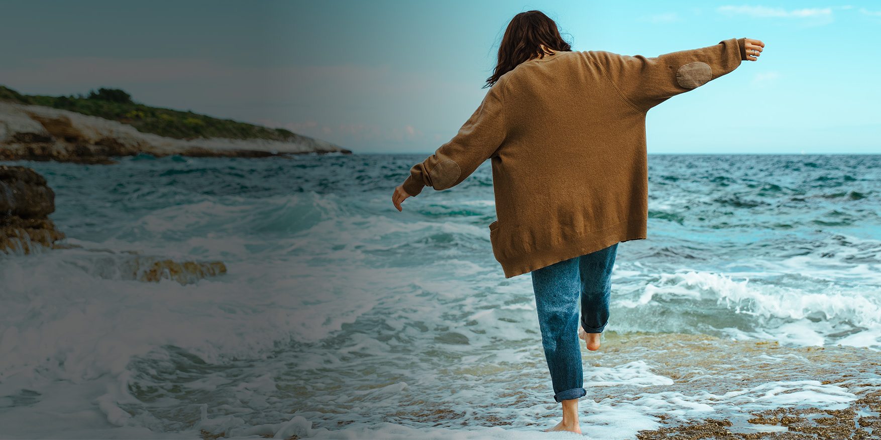 woman walking by rocky sea beach at sunny windy day. summer vacation