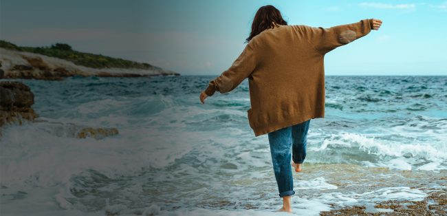 woman walking by rocky sea beach at sunny windy day. summer vacation