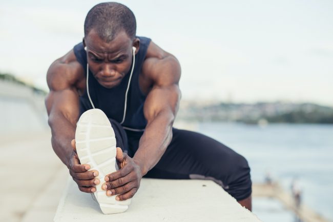 stretching before running in urban background. Young male exercising listening to music with headphones.